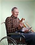 1960s SMILING SENIOR MAN SITTING IN WHEELCHAIR WITH CRUTCHES READING INSURANCE CHECK