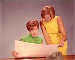 1960s TWO WOMEN EXECUTIVES AT DESK WITH TELEPHONE LOOKING AT WORKSHEET