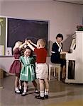 1970s CHILDREN PLAYING LONDON BRIDGE MUSICAL GAME WITH TEACHER PLAYING PIANO NOSTALGIA