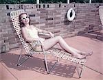 1950s SMILING WOMAN WEARING SUNGLASSES SUN BATHING IN DECK CHAIR CHAISE LOUNGE