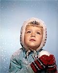 1960s LITTLE GIRL HOLDING SNOW BALL LOOKING SAD UP AT THE SKY RED MITTENS WHITE KNIT HAT BLUE JACKET