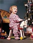 1960s TODDLER GIRL ON WHEELED TOY RIDING HORSE NEAR CHRISTMAS TREE LIVING ROOM HAPPY SMILING