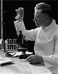 1920s 1930s 1940s SCIENTIST LAB TECHNICIAN IN WHITE COAT LOOKING AT TEST-TUBE IN FRONT OF MICROSCOPE