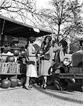 1920s COUPLE WOMEN MAN AT ROADSIDE PRODUCE STAND BUYING PUMPKINS