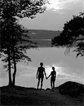 1930ER JAHRE HINTEN ANZEIGEN SILHOUETTE VON MANN UND FRAU IN BADEN-ANZÜGE, DIE HAND IN HAND BEOBACHTEN SONNENUNTERGANG AM SEE