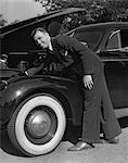 1939 1940s SMILING MAN WEARING SUIT AND TIE CHECKING ENGINE UNDER AUTOMOBILE HOOD