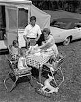 1960s FAMILY OF FIVE HAVING A PICNIC BESIDE THEIR PARKED CAR AND CAMPER TRAILER