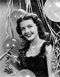 1940s 1950s SMILING WOMAN BLACK PARTY DRESS PEARLS HOLDING NEW YEAR PARTY NOISE MAKER STREAMERS BALLOONS BACKGROUND