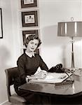 1950s RECEPTIONIST SEATED AT DESK WITH NOTE PAD & PENCIL BEHIND INFORMATION SIGN