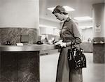 1950s 1960s WOMAN HANDBAG ON ARM GLOVES FILLING OUT DEPOSIT SLIP BANK COUNTER