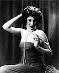1920s WOMAN WEARING STRAPLESS GOWN AND STRING OF PEARLS HOLDING LONG CIGARETTE HOLDER WITH OTHER HAND ON BACK OF HEAD