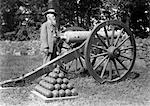 1890s 1900s ELDERLY BEARDED MAN CONFEDERATE CIVIL WAR VETERAN WITH MILITARY DECORATIONS ON COAT STANDING NEXT TO CANNON