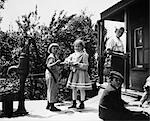 1890s 1900s TURN OF THE CENTURY GROUP OF CHILDREN STANDING ON FRONT PORCH TWO GIRLS PLAYING BY WATER PUMP