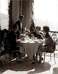 1920s GROUP EATING ON BALCONY WITH WAITER SERVING WINE