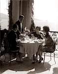 1920s GROUP EATING ON BALCONY WITH WAITER SERVING WINE