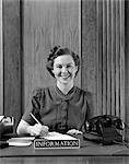 1940s PORTRAIT OF SMILING WOMAN INFORMATION DESK RECEPTIONIST HOLDING PENCIL OVER APPOINTMENT BOOK