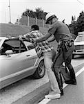 1970s POLICEMAN SEARCHING AFRICAN AMERICAN MAN SPREAD EAGLE AGAINST CAR
