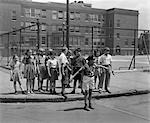 1930s PATERSON NJ BOY CROSSING GUARD HOLDING BACK GROUP OF ELEMENTARY SCHOOL STUDENTS WAITING AT CURB TO CROSS STREET