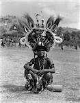 1920s 1930s PORTRAIT NATIVE MAN IN ELABORATE FEATHERED HEADDRESS COSTUME SITTING ON GROUND PORT MORESBY NEW GUINEA