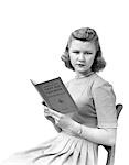 1940s WOMAN SEATED FACING VIEWER WHILE HOLDING A BOOK ENTITLED FIRST AID TEXTBOOK