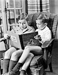 1950s TWO BOYS SITTING IN ONE CHAIR SHARING LARGE BOOK ARMCHAIR