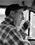 1970s SIDE VIEW OF TRUCKER IN PLAID FLANNEL SHIRT & BASEBALL CAP USING CB RADIO