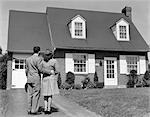 1940s COUPLE LOOKING AT SUBURBAN HOUSE