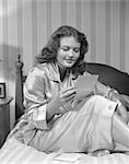 ANNÉES 50 DES ANNÉES 1940 JEUNE FEMME EN SOURIANT LIRE LIT UNE LETTRE ENVOYÉE PORTER DES PYJAMAS DE SOIE RAYÉ WALLPAPER