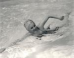 1960s SMILING WOMAN IN FANCY BATHING CAP IN MID-STROKE SWIMMING IN POOL
