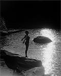 1920s SILHOUETTE OF WOMAN IN BATHING SUIT STANDING ON A ROCK NEAR WATER