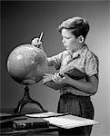 1940s 1950s SERIOUS BOY FINDING LOCATION ON WORLD EARTH GLOBE WITH PENCIL HOLD OPEN BOOK GEOGRAPHY