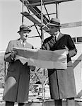 1960s TWO BUSINESSMEN REVIEWING BLUEPRINTS AT CONSTRUCTION SITE OUTDOOR