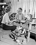 1960s MOTHER DAUGHTER SHOE SHOPPING SALESWOMAN SHOWING PATENT LEATHER SHOE TO GIRL IN RETAIL STORE