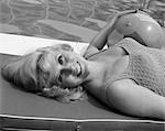 1960s CLOSE-UP OF BLOND BATHING BEAUTY LYING FLAT ON BACK ON RAFT IN POOL WITH BEACH BALL UNDER ARM TURNING HEAD TOWARD CAMERA