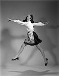 1960s WOMAN HOUSEWIFE WEAR APRON JUMP JUMPING IN AIR BLACK SKIRT WHITE BLOUSE HAPPY SMILING JOY GOOFY WACKY EXPRESSION CHARACTER