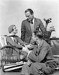 1930s TWO MEN ONE WOMAN GOLF CLUBS AND BAG SMILING TALKING SITTING BAMBOO CHAIR MAN SMOKING PIPE
