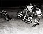 1950s HOCKEY GAME WITH ONE OF 4 PLAYERS IN FOREGROUND BEING KNOCKED DOWN BY 2 OPPOSING TEAM MEMBERS