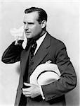 1930s MAN IN SUIT HOLDING HAT WIPING FACE WITH HANDKERCHIEF