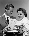 1950s SMILING PORTRAIT COUPLE LOOKING AT COPY OF NEW MORTGAGE