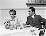 1930s QUARRELING COUPLE AT A TABLE SET FOR BREAKFAST THE WOMAN IS WEARING PRINT DRESS BOW