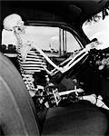 1930s 1940s STILL LIFE OF SKELETON DRIVING CAR WITH WHISKEY BOTTLE AND WOMAN'S SHOES ON SEAT BESIDE IT