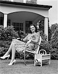 1940s WOMAN HOLDING BOOK SMILING AT CAMERA SITTING IN LAWN CHAIR MAGAZINE RACK PORCH HOUSE