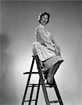 1950s WOMAN IN APRON SITTING ON LADDER WITH EXAGGERATED EXPRESSION