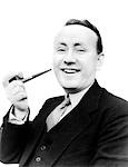 1940s PORTRAIT MAN HOLDING PIPE IN HIS HAND SMILING AT CAMERA DRESSED IN SUIT AND TIE SMOKING BAD HABIT TOBACCO