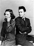 1930s 1940s YOUNG COUPLE GIRL TALKING ON TELEPHONE BOY ARMS CROSSED LOOKS ANNOYED