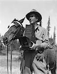 1940s MAN IN FEDORA & JODHPURS STANDING NEXT TO SADDLED HORSE HOLDING GRAFLEX CAMERA