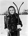 1930s LITTLE GIRL STANDING HOLDING SKIS AND POLES SMILING