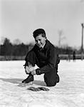 1920s 1930s BOY TYING ICE SKATE LACE KNEELING ON ICE LOOKING AT CAMERA