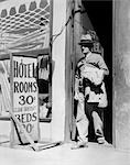 1940s ELDERLY MAN WALKING OUT OF DOOR NEXT TO SIGN READING HOTEL ROOMS 30 CENTS CLEAN SANITARY BEDS 20 CENTS