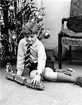 1930s YOUNG BOY PLAYING WITH TOY TRAIN BY CHRISTMAS TREE